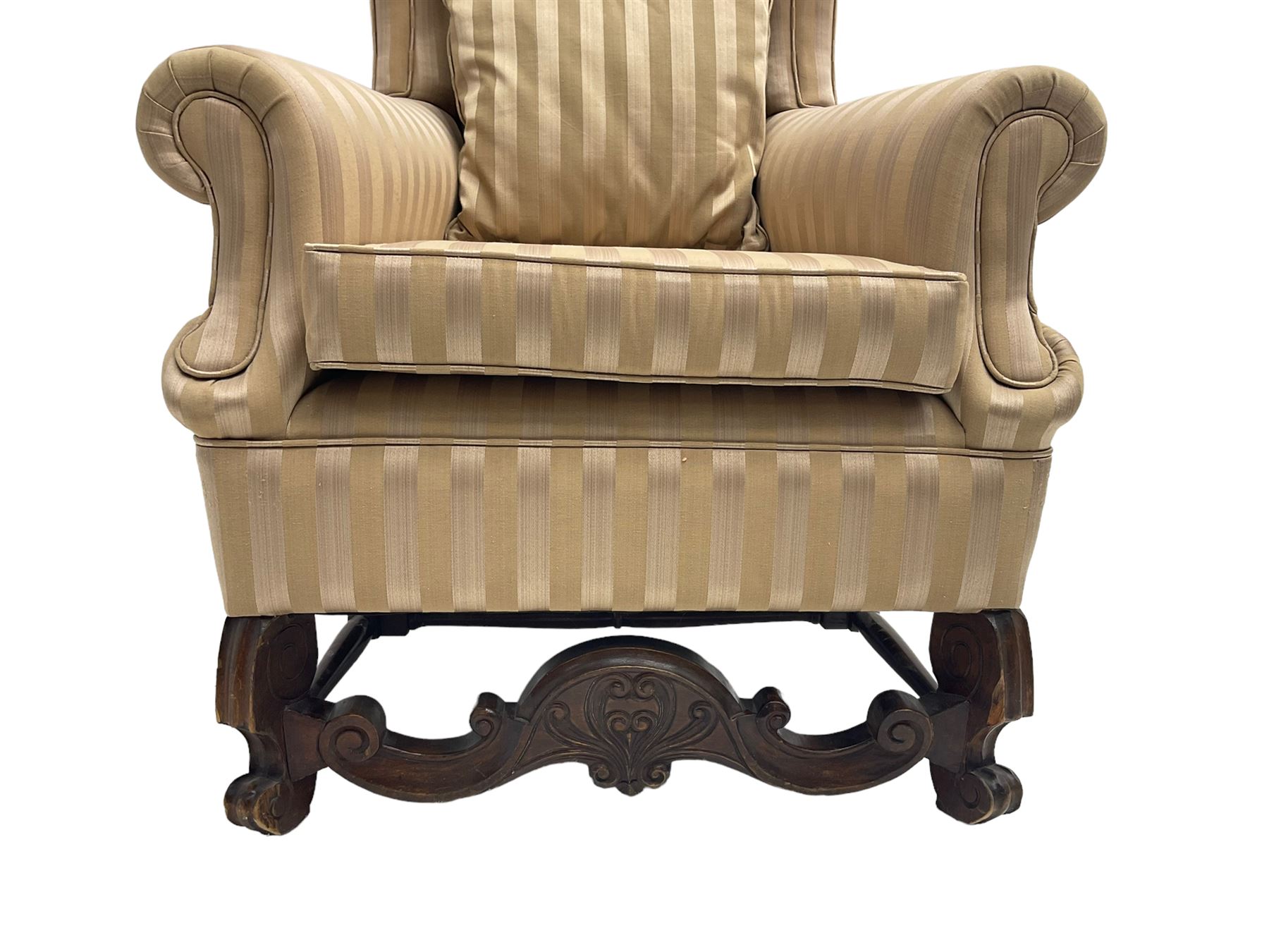 William and Mary style wingback armchair, upholstered in gold striped fabric, on walnut scroll carved supports joined by scroll and foliate carved middle rail, turned H-shaped stretchers, on castors