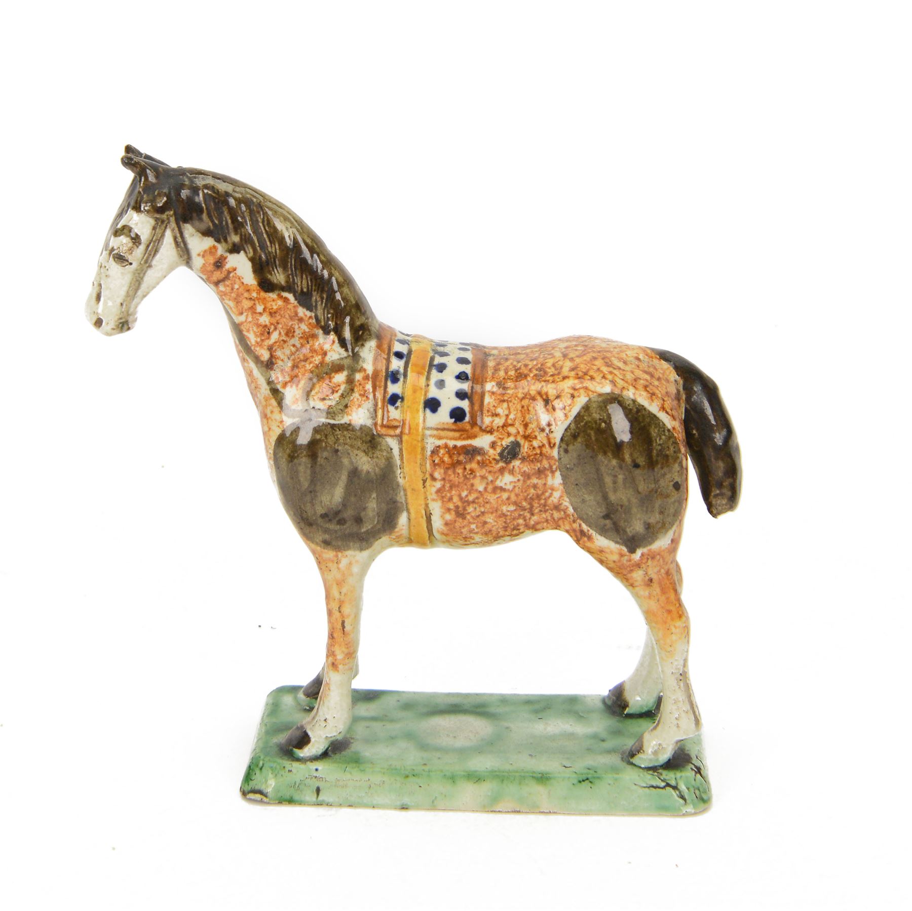 Late 18th/early 19th century Prattware pottery figure of a horse, possibly Yorkshire Potteries, circa 1790-1800, painted and sponge decorated in manganese, with blue spotted saddle secured with a yellow girth, upon a rectangular green base, H15.5cm