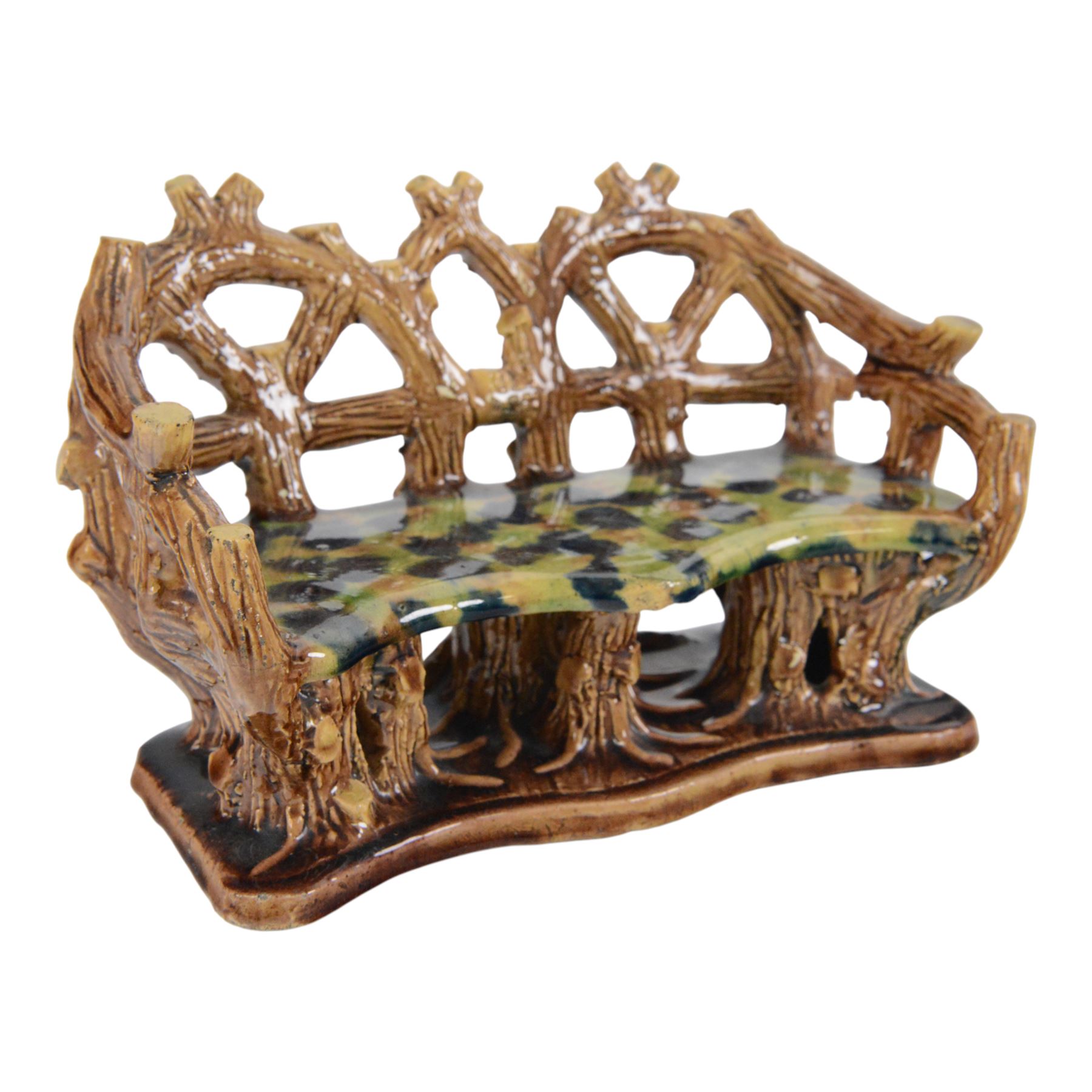 19th century pottery model of a bench, possibly Skey Pottery Tamworth, Staffordshire, the shaped seat mottled in shades of green, dark blue, yellow and brown, supported upon naturalistically modelled tree stumps, the arms and back modelled as intertwined branches, H14cm W21cm D10cm