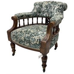 Victorian walnut framed tub-shaped armchair, the shaped rolled back supported by a spindle turned balustrade, upholstered in buttoned floral fabric, scrolled arms supports carved with acanthus leaves and flower heads, on collar turned feet with brass and ceramic castors