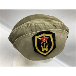 Four side caps - WW2 Russian, post-WW2 Russian and two East German; all with badges, one with multiple metal badges (4)