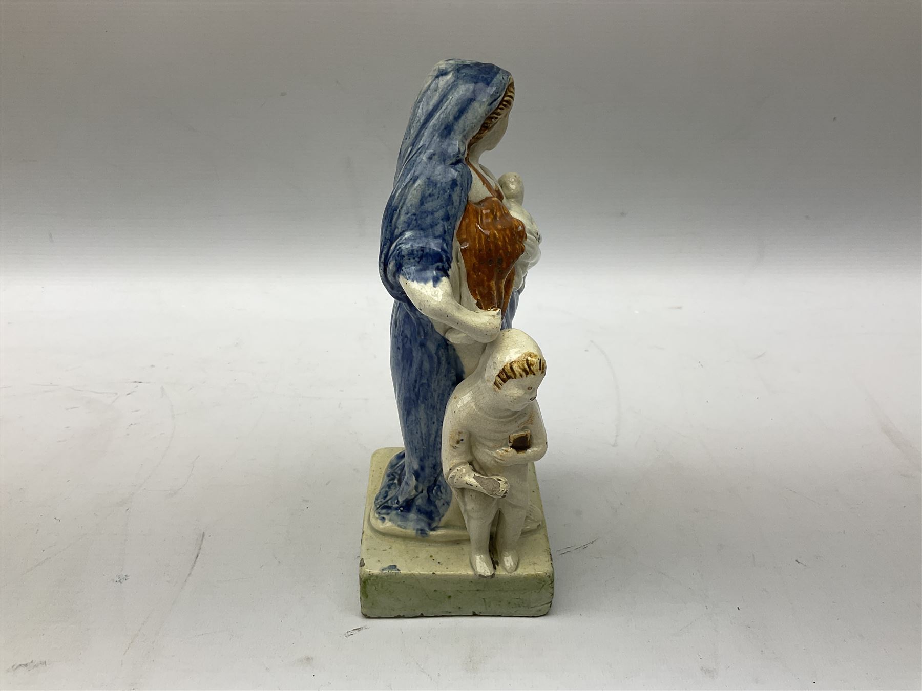 Late 18th century Prattware figure representing Charity, modelled as a mother with baby in her arms and two small children clutching at her robes, upon a square base, overall H21cm.