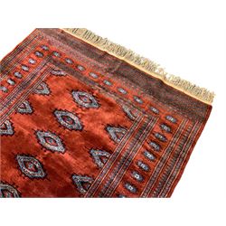 Persian Bokhara burnt amber ground rug, the field decorated with indigo lozenge shaped Gul motifs, within a guarded border of further repeating Gul designs
