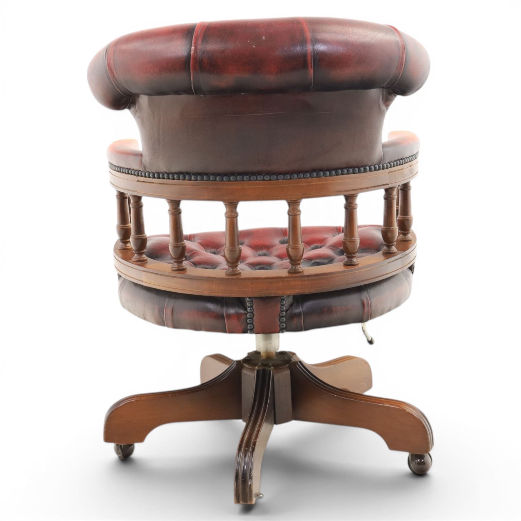 Captains swivel desk chair upholstered in oxblood leather, buttoned back and seat, shaped arm bow raised on turned spindles, five spoke base raised on castors