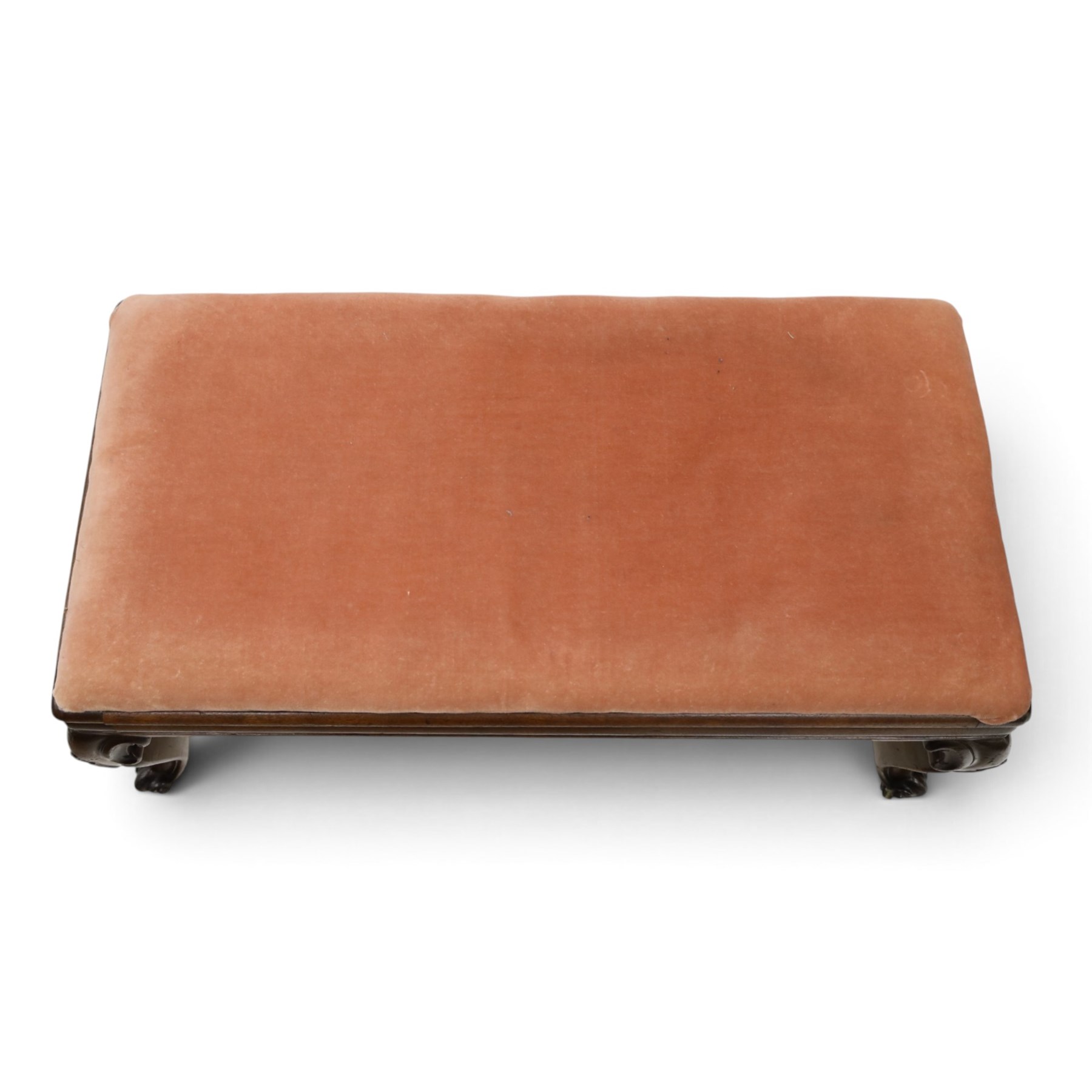 Victorian carved mahogany fender stool of generous proportions, the wide rectangular seat upholstered in rose fabric, shaped frieze rail over C-scroll and cartouche carved cabriole supports with scroll feet and brass castors