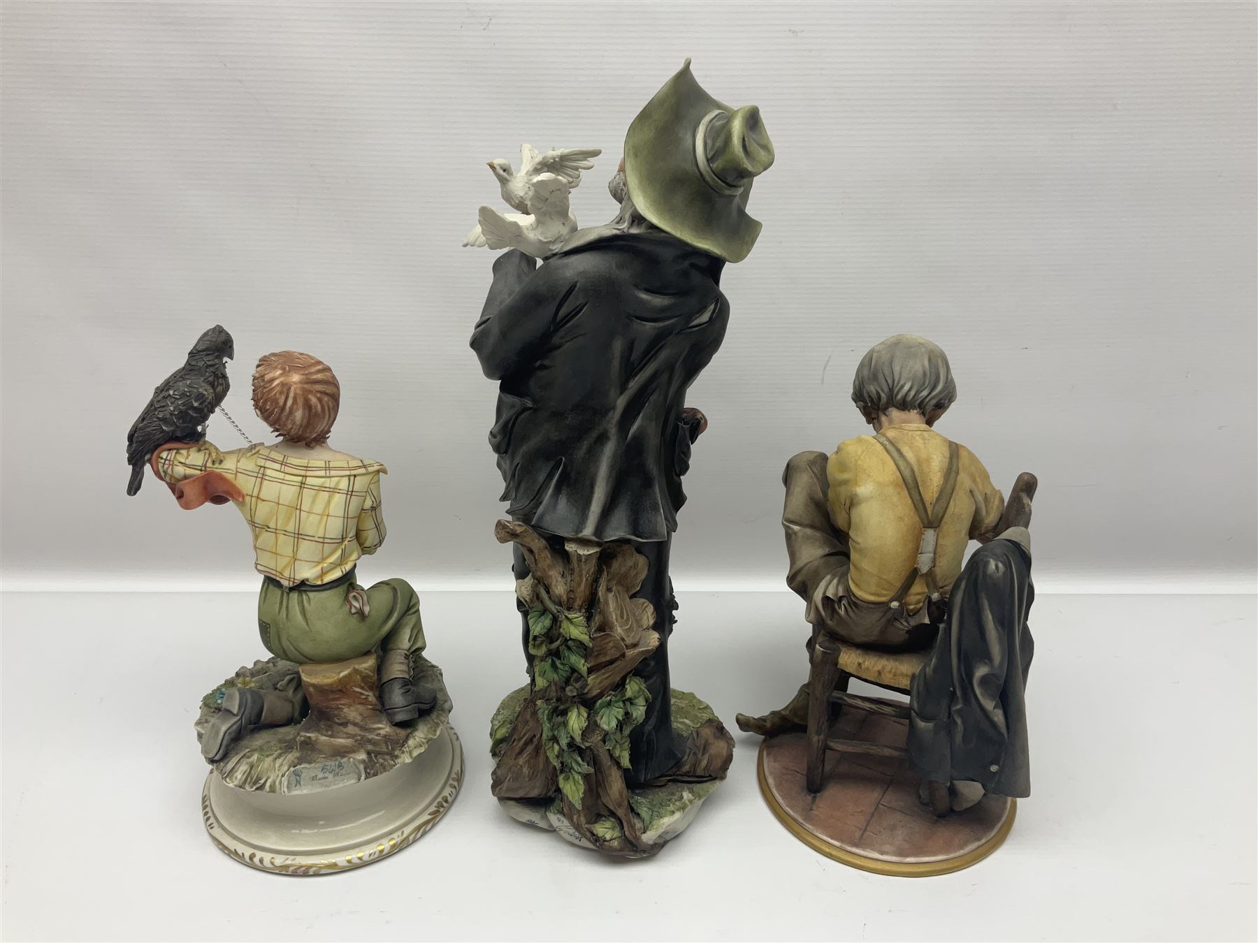 Three Capodimonte figures, to include The Kind Heart Man, modelled by Cortese as a tramp with two doves, The Young Falconer by Maria Angela and another modelled as a tramp darning his socks, all with printed marks, tallest H39cm