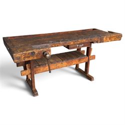 Large early 20th century rustic stained reclaimed pine workbench, the substantial plank top with recessed tool well and two homemade wooden screw vices, above a single frieze drawer and slatted undertier, raised on trestle end supports