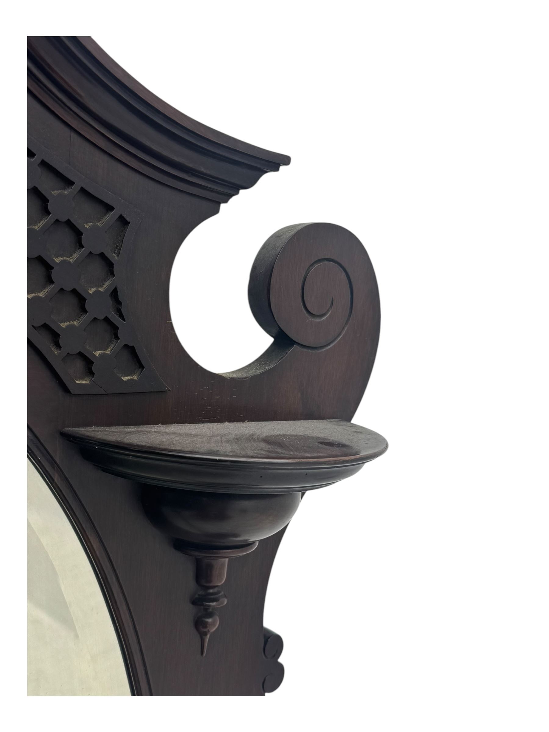 Early 20th century mahogany overmantel mirror, shaped broken pediment crest with open lattice panels, oval mirror plate flanked by scroll-carved bracket shelves

