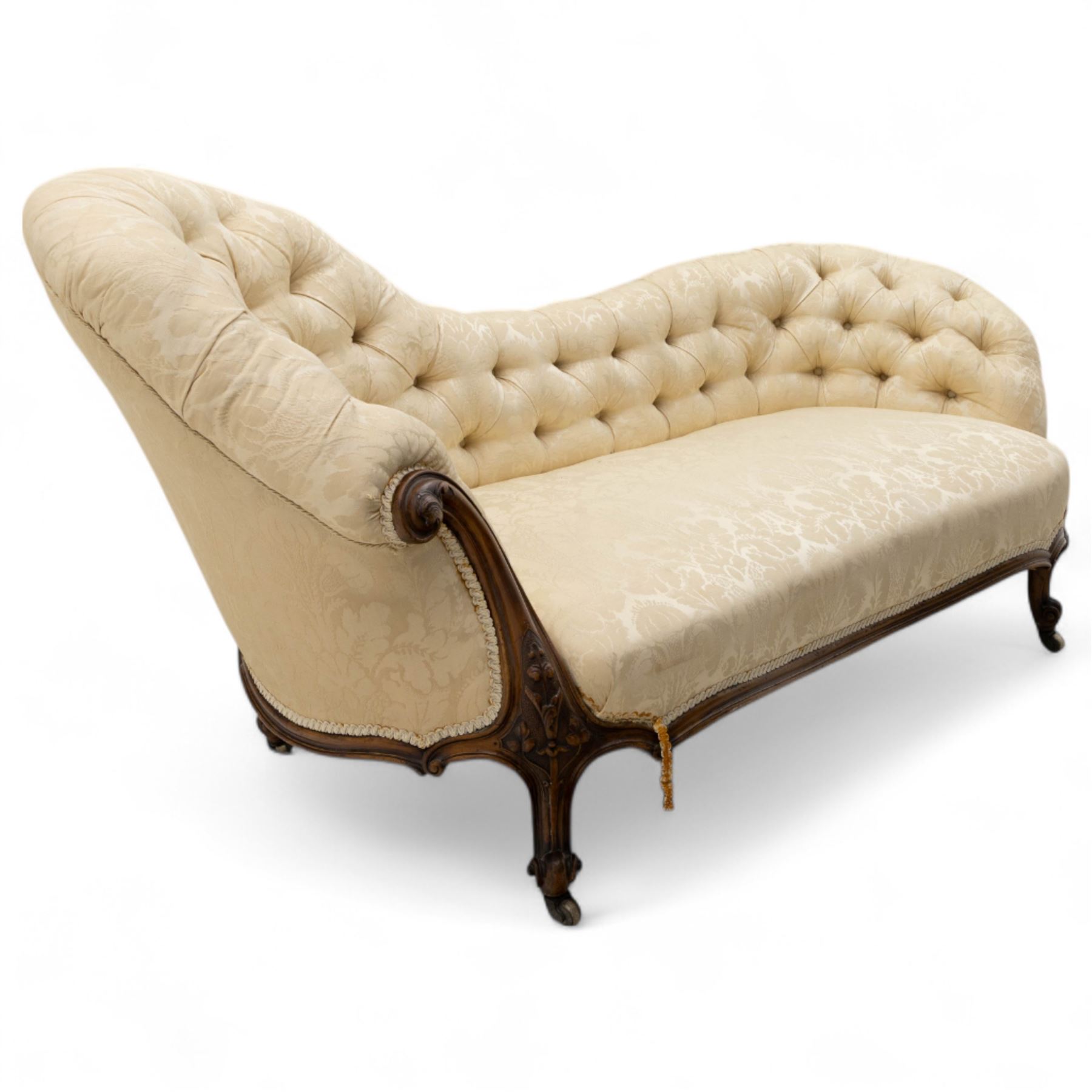 Late 19th century Victorian walnut button-back recamier, asymmetrical form, with cream damask fabric and gimp braid edging, shaped reeded apron above front and back scroll carved cabriole legs on brass castors
