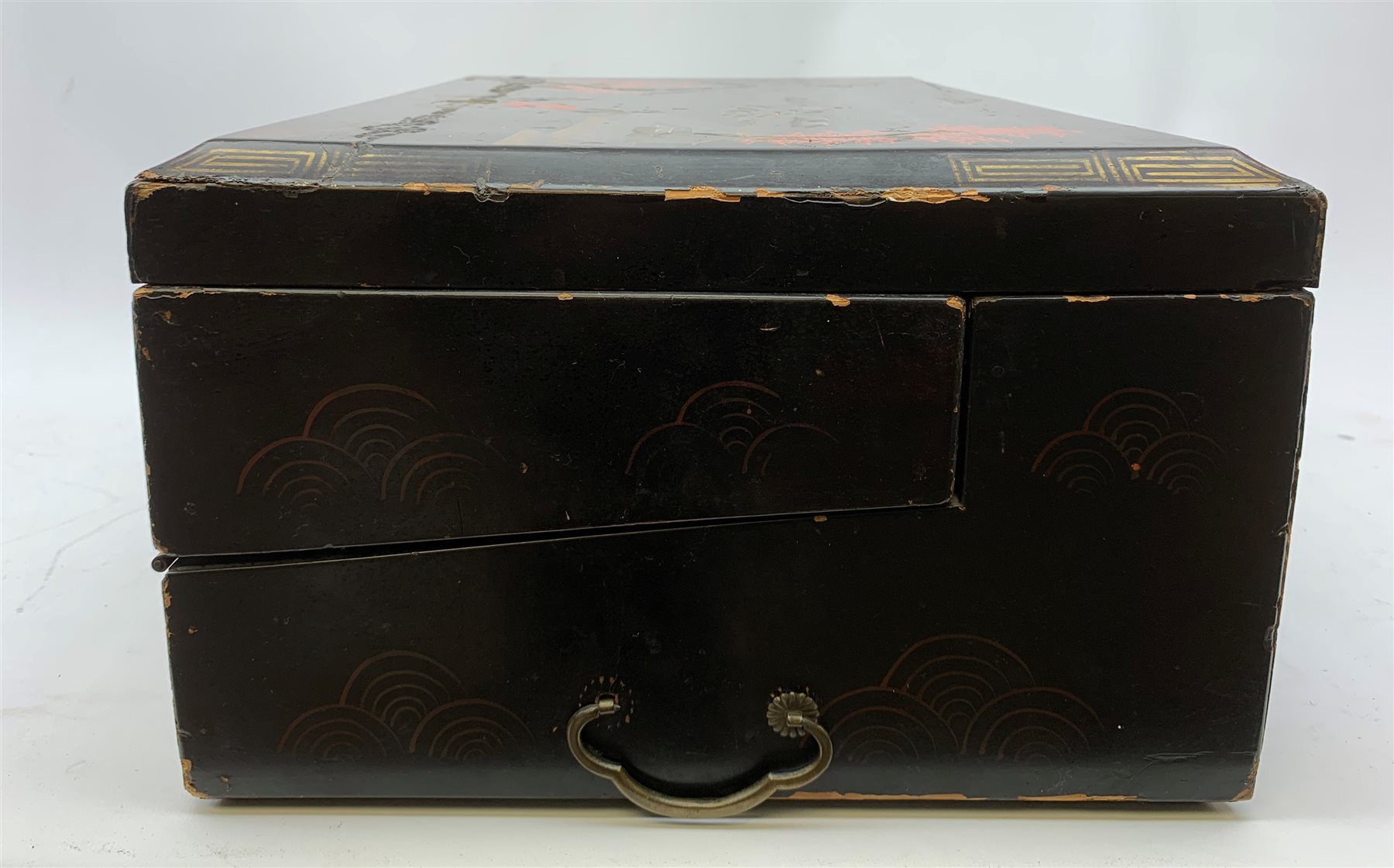  A 20th century Chinese black lacquer and gilt detailed writing box, decorated with figures, pagodas and cranes amidst a mountainous landscape, the hinged cover opening to reveal a compartmented interior and fold out baize lined slope, H20cm L46.5cm D31.5cm.   