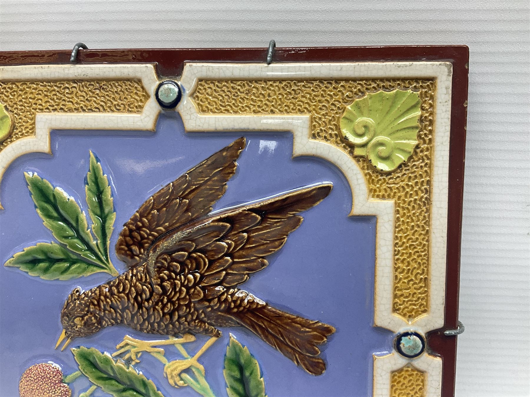 19th century Minton & Co majolica tile, decorated in relief with a bird upon a fruiting branch against a blue ground, with textured ochre border and anthemion to each corner, impressed mark verso, H19.7cm