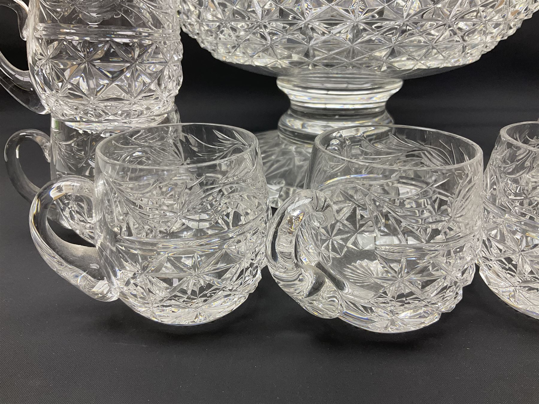 Large Stuart crystal pedestal punch bowl, of circular form, the rim with engraved floral decoration, upon spreading circular foot with radial cut decoration, with seven matching Stuart crystal drinking glasses, each with a C handle, each acid signed beneath, bowl H20cm