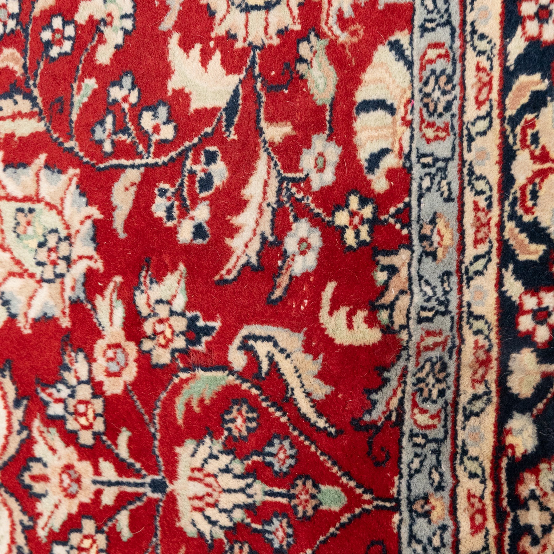 Persian crimson ground rug, interlacing floral stems linking ivory palmettes, rosettes and serrated leaves, within a navy floral border flanked by ivory patterned guards