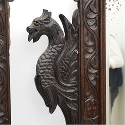 Late Victorian heavily carved oak hall stand, the scrollwork pediment with carved lion's head, bevelled mirror plate flanked by carved dragon motifs, over hinged storage compartment and umbrella stands with drip trays, on turned front supports