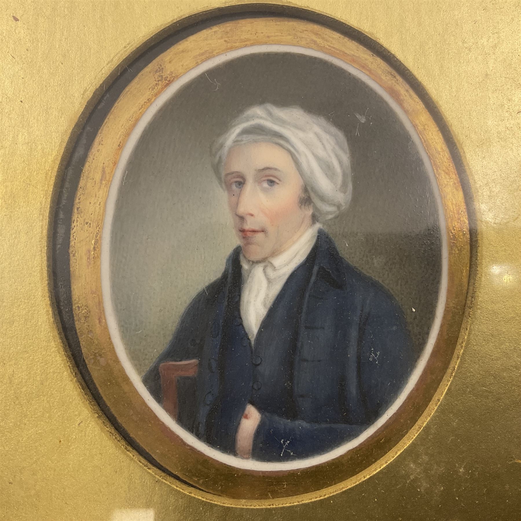 English School (18th century)
Portrait miniature upon ceramic plaque 
Head and shoulder portrait of a gentleman in blue coat and white turban, holding book under one arm
Indistinct inscription verso
Within gilt mount and gilt frame under glass
Portrait 7cm x 5.5cm 
Plaque 14cm x 11.5cm
Frame 16cm x 13.5cm