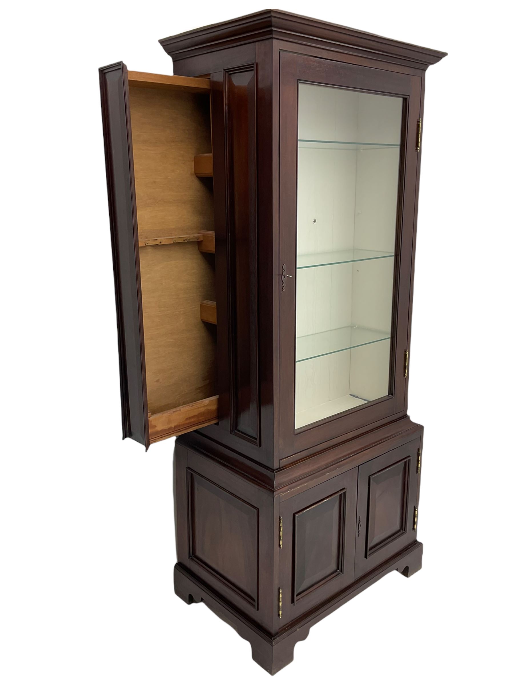 Mahogany display cabinet with hidden compartment, projecting cornice over single glazed door enclosing glass shelves, double panelled cupboard below, the interior with button releasing sliding back compartment, on bracket feet