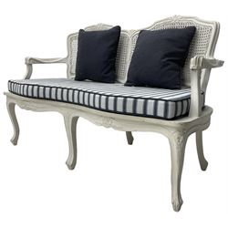 French design white painted two seat serpentine settee, floral carved cresting rail over cane back, loose striped upholstered seat cushion, on cabriole supports