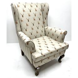 Wingback armchair upholstered in a grey fabric decorated with stags, cabriole feet, scrolling arms