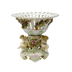  German Sitzendorf porcelain centrepiece, the pierced basket applied with fruit and trailing flowers, the stem supported by three cherubs on scrolled supports, H31cm   