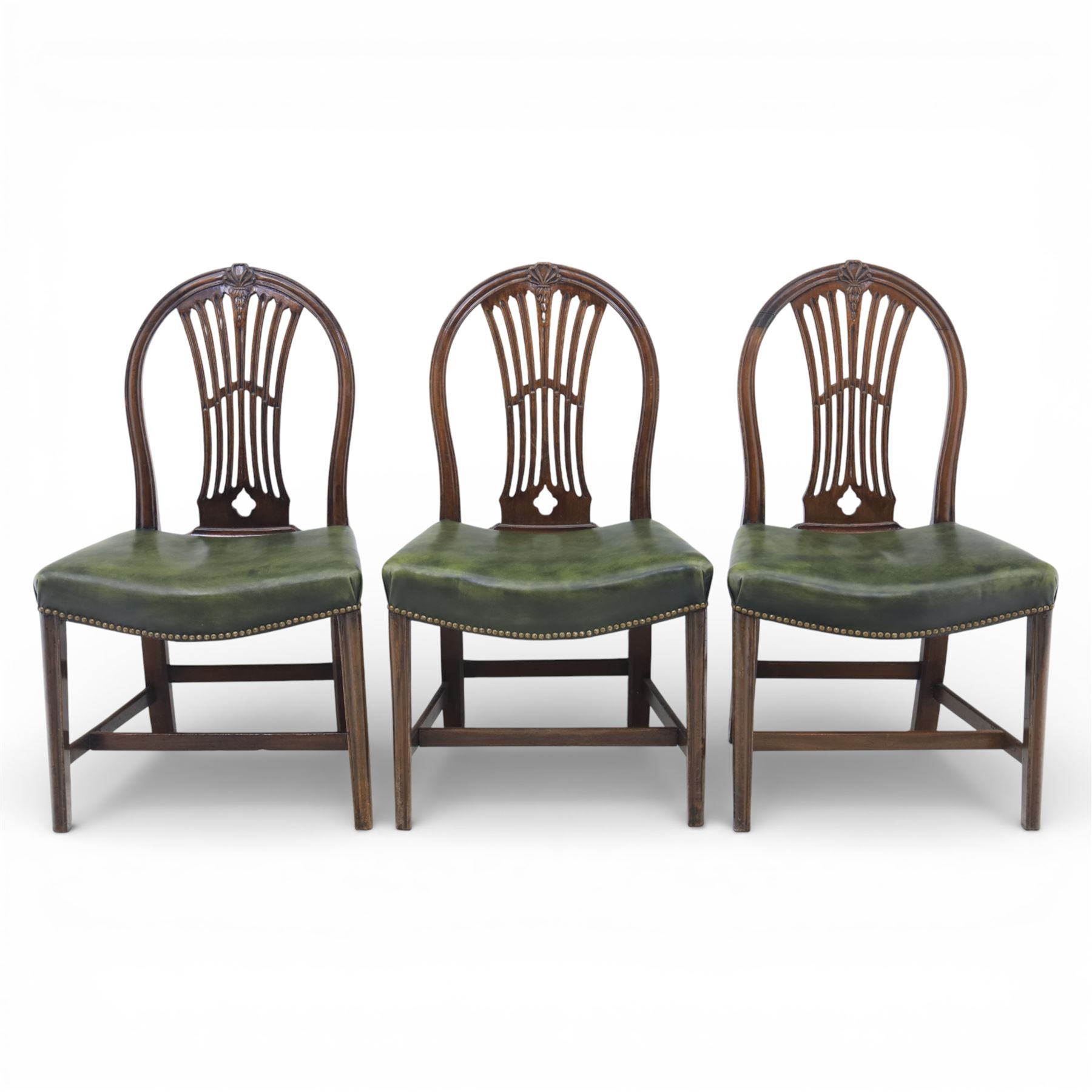 George III style set of six mahogany dining chairs, the arched backs with pierced and carved vase splats beneath carved husk and patera detail, drop-in upholstered seats covered in green leather with brass studded edging, raised on square section legs united by plain stretchers