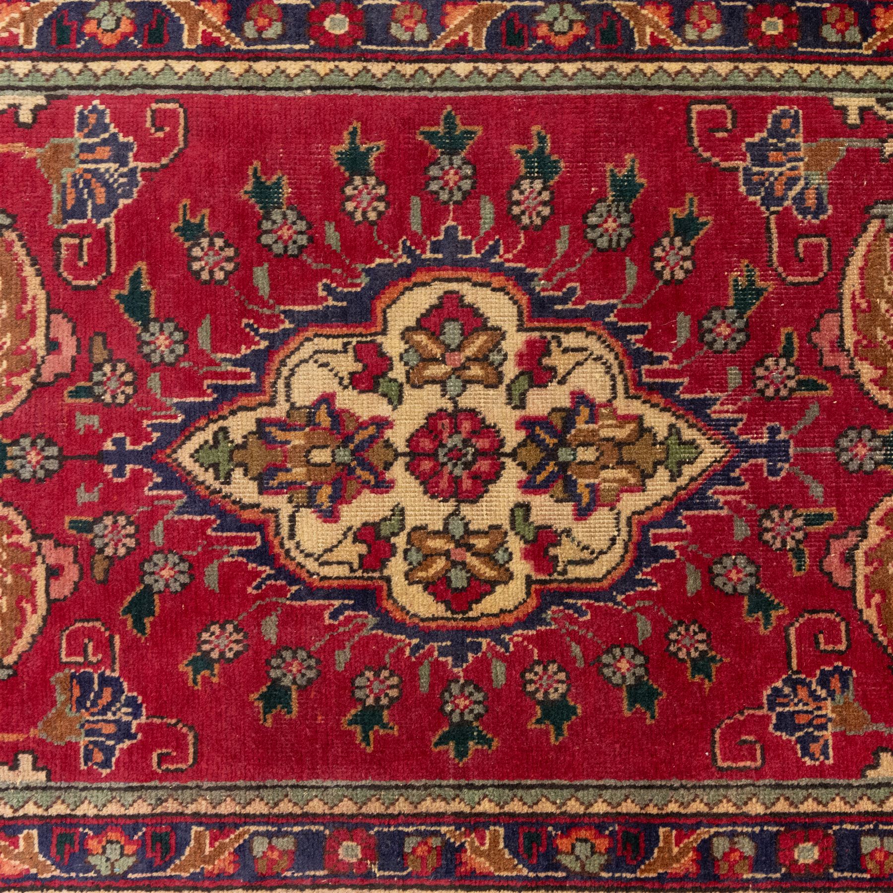 North West Persian Tabriz hand-knotted runner, madder red field with central octagonal medallions of sage green, navy and ivory, ground enclosing a floral rosette and radiating angular vinery, scrolling floral sprays and palmettes either end with shaped pendants principal border on navy ground decorated with a continuous vine-scroll of palmettes and rosettes, flanked by narrow guard borders, with cotton fringe ends 
