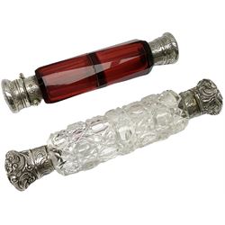 Two Victorian white metal mounted double ended scent bottles, comprising a ruby glass example with scroll engraved covers, L13cm, and an octagonal and hobnail cut glass example with foliate and scroll embossed covers, L15cm.