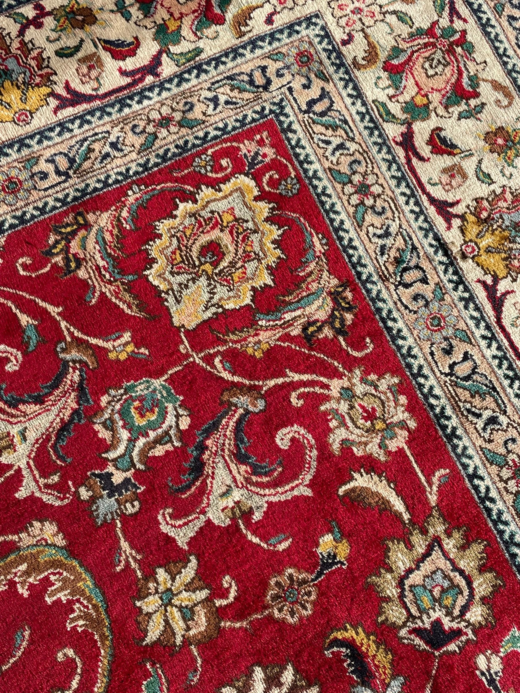 Persian Tabriz crimson ground carpet, decorated with swirling leafy branches and large palmette motifs, the pale ground border decorated with trailing foliate pattern, within floral guard stripes