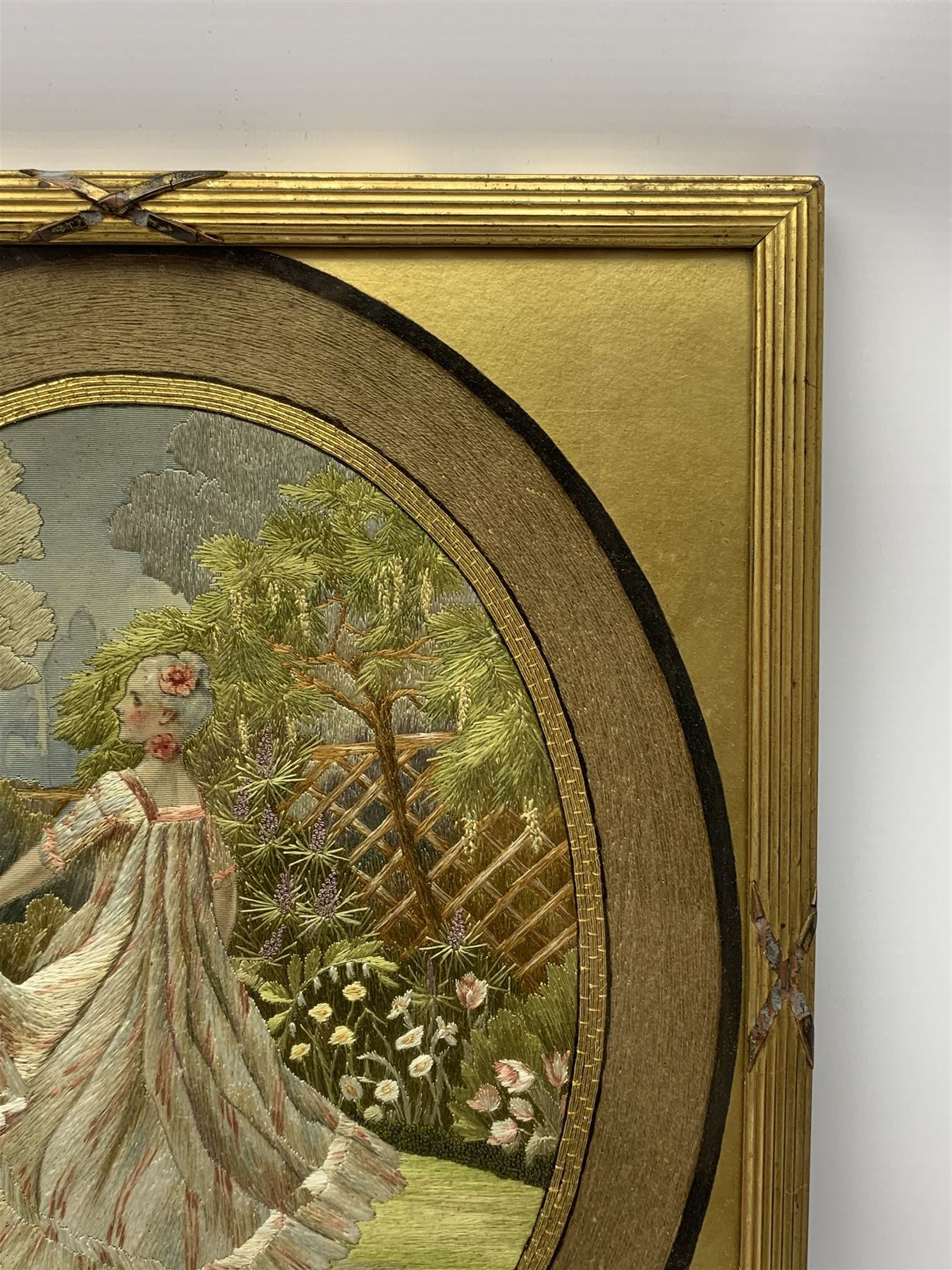 George III silkwork picture, of oval form depicting a female figure in garden setting, within a silkwork border detailed with verse from Robert Burns Bonnie Peg, 'Her air sae sweet, and shape complete, The Queen of Love did never move, Wi' Motion mair enchanting!', and monograms 'FV' and 'SM', in reeded gilt frame and gilt mount, indistinctly inscribed in pencil verso, overall H36cm L30.5cm