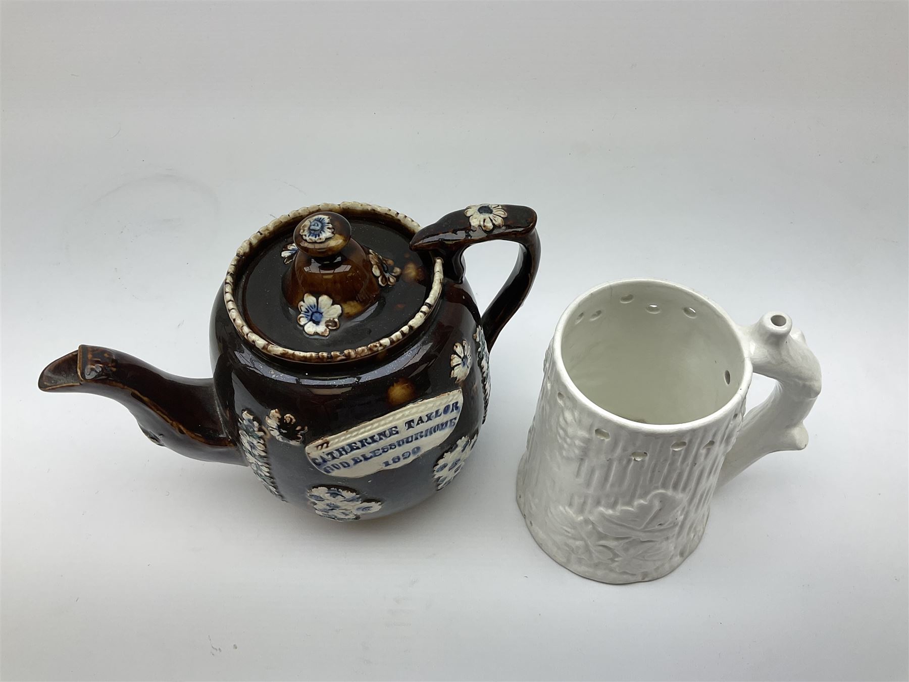 A 19th century Barge Ware teapot, decorated with applied floral sprays and thistles against a mottled brown ground, and plaque detailed Catherine Taylor God Bless Our Home 1890, H18cm, together with a white glazed puzzle mug, H15cm. 