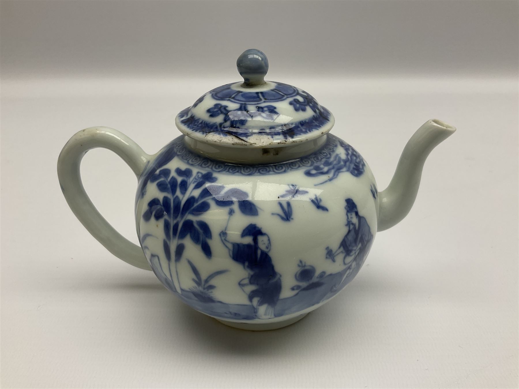 Two late 18th/early 19th century Chinese export teapots, the largest example of globular form with curved handle and straight spout, decorated in the Mandarin style with figural scenes surrounded by red scale reserves, H13.5cm, the second smaller example decorated in underglaze blue with two musicians in a landscape set with willow tree and fence, H10.5cm

