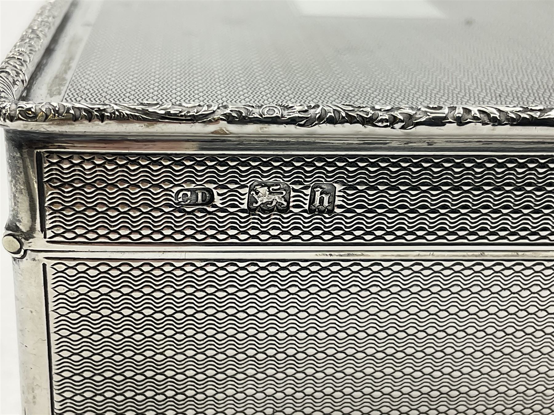 1920's silver table cigarette box, of rectangular form with engine turned decoration to the exterior, the hinged cover with central vacant rectangular panel and raised foliate rim, opening to reveal a gilt interior with later plush lining, hallmarked Charles Henry Dumenil, London 1923, H3.5cm L14.5cm D8.5cm