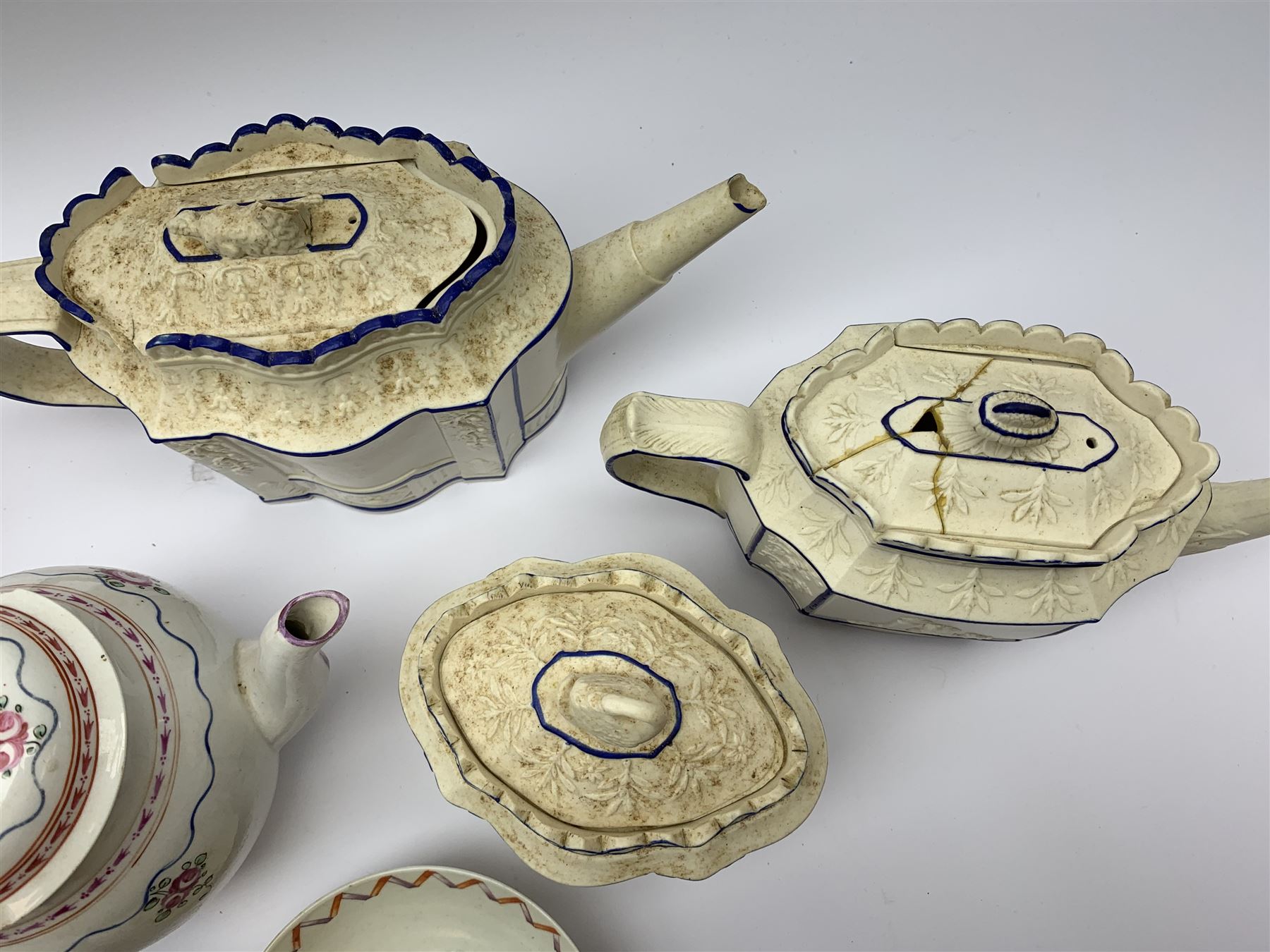 Two19th century relief moulded Castleford teapots, and lidded sucrier, largest teapot H14.5cm, together with three 18th century New Hall type teapots, an early 18th century saucer, and an 18th century blue and white bowl.