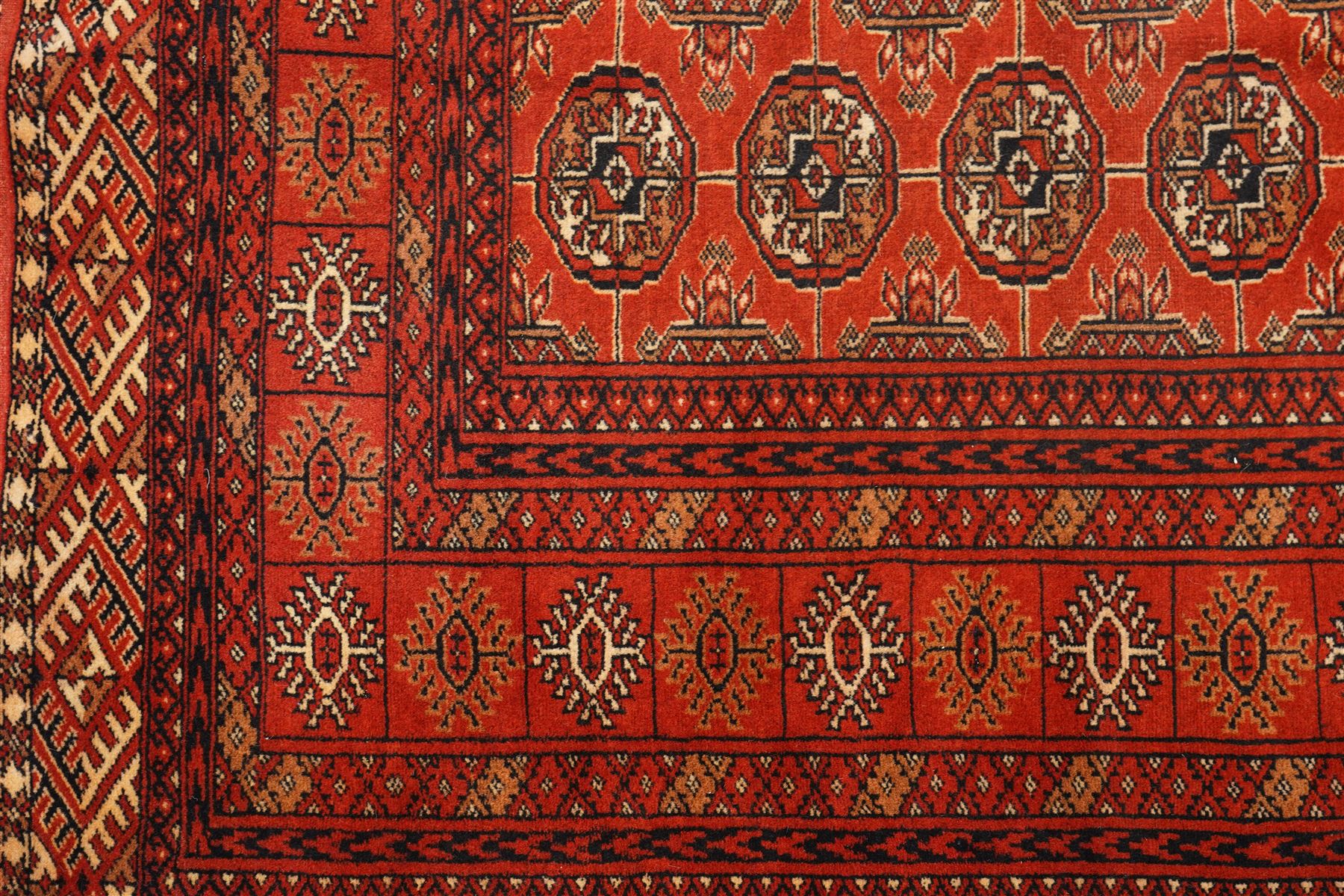 Turkmen hand-knotted carpet, madder red field, with an all-over design of row of Tekke guls, each enclosing stylized cruciform and geometric devices in tones of ivory, dark brown, and indigo, principal border of stylized geometric motifs, flanked by guard border with angular latch hook geometric designs, with cotton fringe ends 