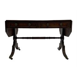 Regency mahogany sofa table, canted rectangular drop leaf top with walnut crossbanding, fitted with two frieze drawers with central lozenge decoration, two opposing false drawers, vasiform end supports with reeded edge and central roundel joined by ring turned and reeded stretcher, splayed supports on scaled brass cups and castors