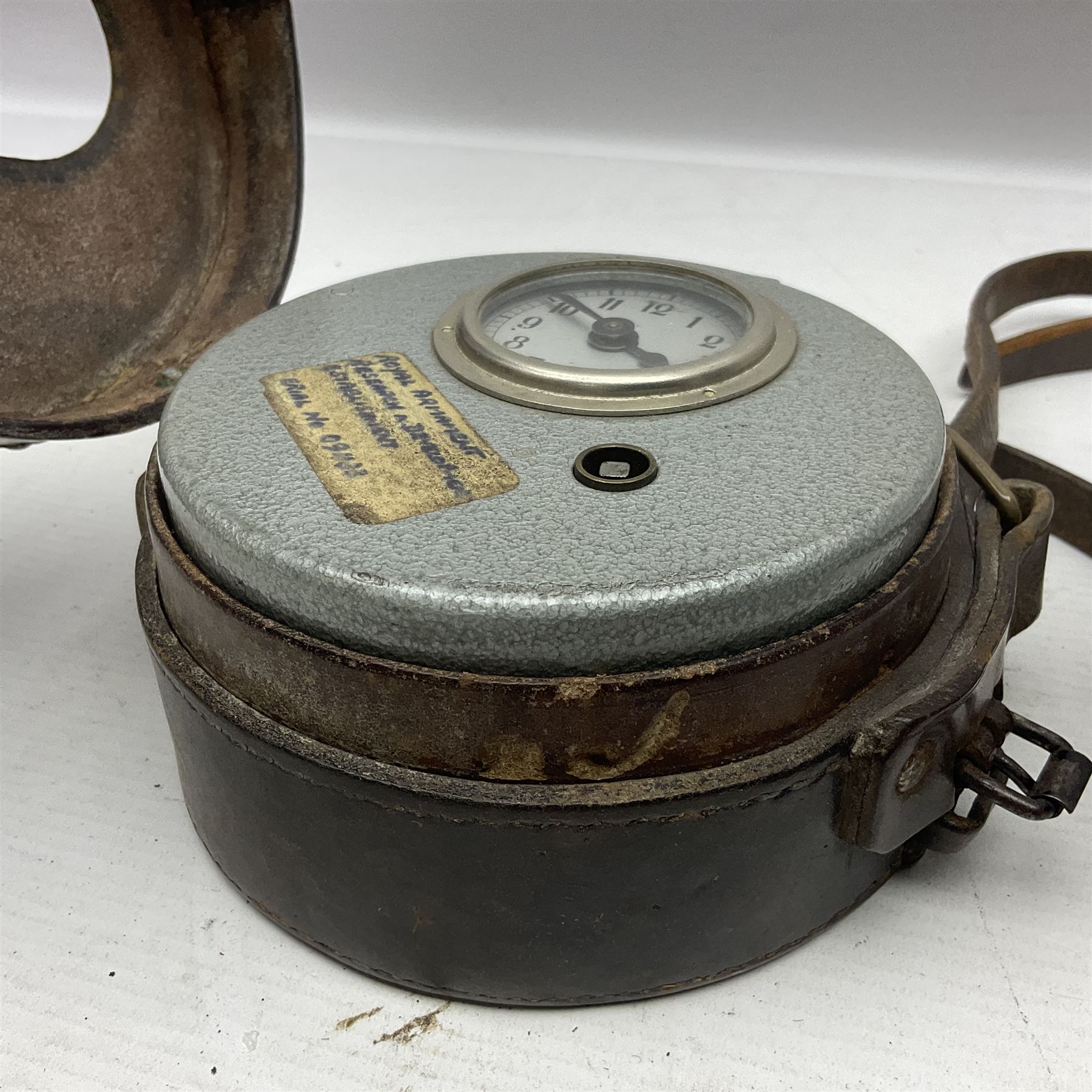 Metal cased drum shaped travelling clock with grey hammered finish, French clockwork movement and stitched leather outer case with shoulder strap; bears manuscript label 'Royal Armament Research and Development Establishment - serial no.09433' D13cm overall