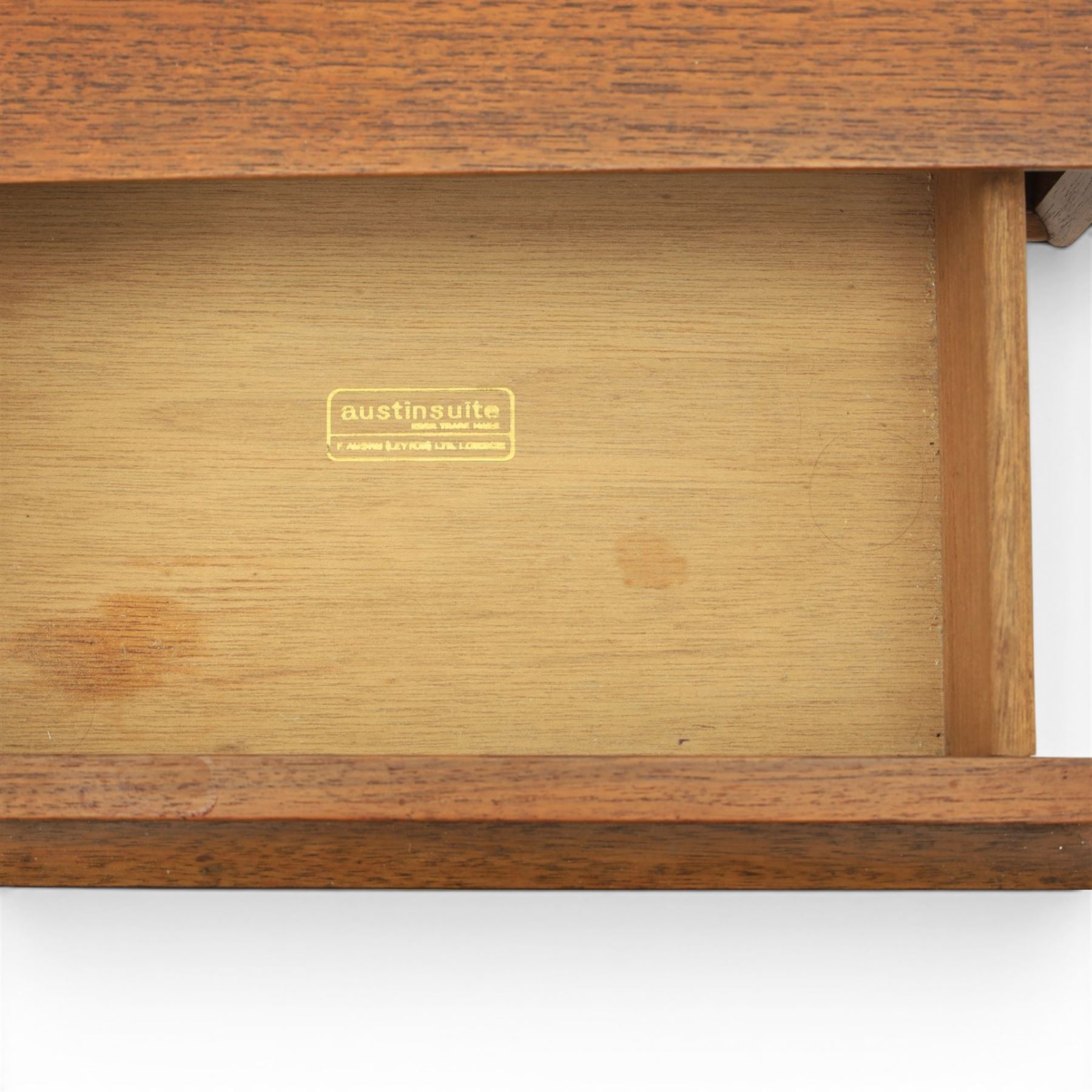 Austinsuite - mid 20th century teak headboard with bedside cabinets and matching  mirrored dressing table, the headboard with floating single drawer bedsides raised on a single tapering support, the dressing table with attached tilting mirror, above rectangular top with kneehole and two banks of two drawers, raised on tapering supports

Headboard H 84cm, D 40cm, W 229cm, W between bedsides 151cm 
Dressing table H 113cm D 44cm, W 149cm, H to underside of dresser 61cm