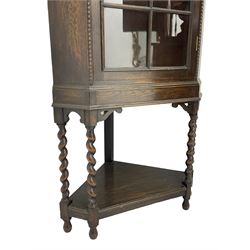 Early 20th century oak corner display cabinet, enclosed by glazed door, on spiral turned supports joined by undertier 