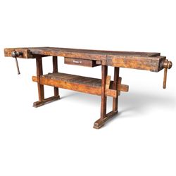 Large early 20th century rustic stained reclaimed pine workbench, the substantial plank top with recessed tool well and two homemade wooden screw vices, above a single frieze drawer and slatted undertier, raised on trestle end supports