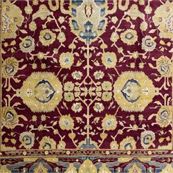 Agra design wool carpet, burgundy field decorated with large scrolling floral vines, palmettes and flowerheads, enclosed by blue main border with oversized stylised palmettes and narrow guard stripes
