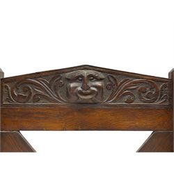 Victorian oak wall hanging whip or stick rack, sloped arch pediment carved with central grotesque mask with extended scrolling foliage, the upright supports cut with rests, x-framed back, two lower hooks