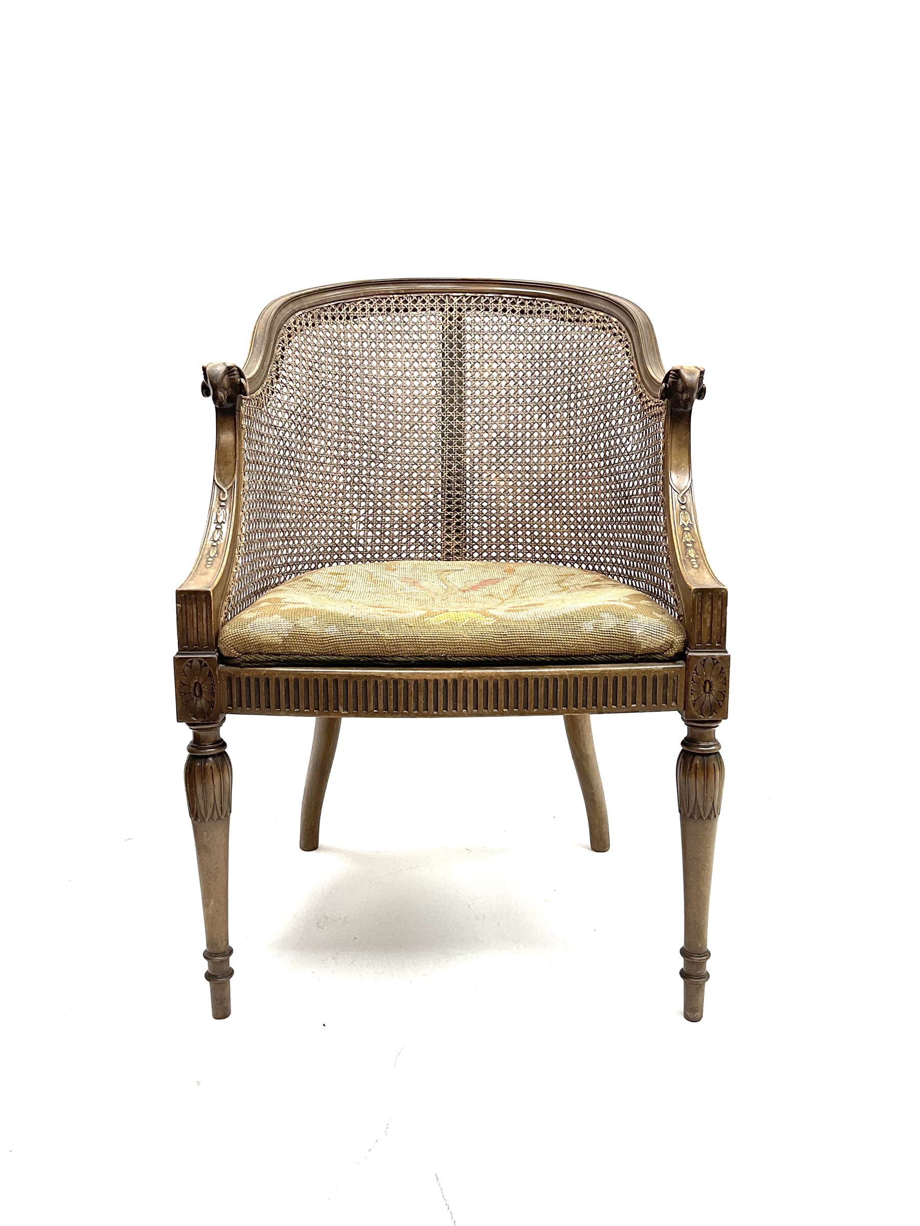 Early 20th century walnut Bergère chair, moulded and shaped frame terminating in rams head, cane woven back meets patterned upholstered seat, raised on leaf carved and fluted supports 