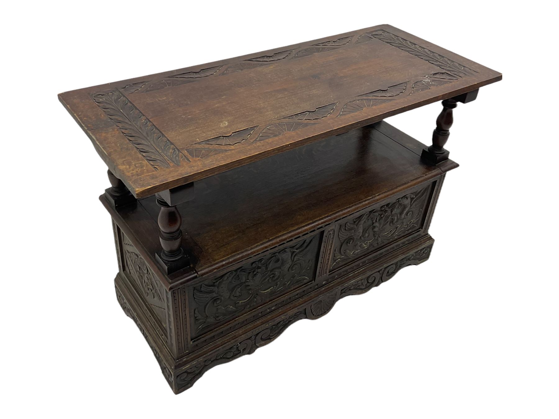 Late 19th century oak monk's bench, the hinged back or top carved with mythical winged dragons, central cartouche and scrolling acanthus leaves, on turned supports, hinged box seat revealing storage, the panelled front matching the back, shaped bracketed skirt carved with shell and scrolled leafage