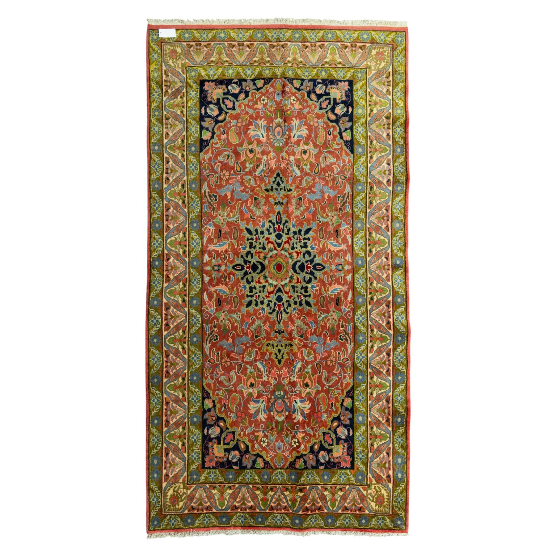 South Persian Sirjan hand-knotted carpet, terracotta ground, with a central shaped dark navy floral medallion with pendants, surrounded by scrolling foliate and floral motifs incorporating palmettes, rosettes and stylised vine work in blue, green and ivory tones, enclosed by dark navy spandrels and a wide green and ivory border with repeating palmettes and angular leaf motifs, flanked by patterned guard stripes, with cotton fringes