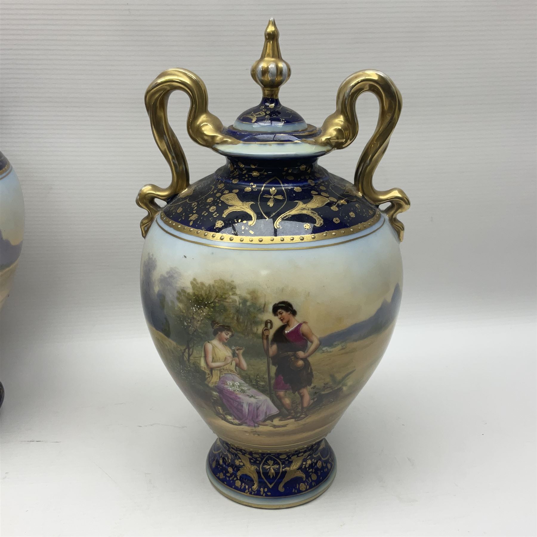 19th century Vienna style porcelain 'Musik' garniture, the central vase of baluster form with domed cover flanked by two smaller vases with twin curved gilt handles to short neck, each decorated with classical figural vignettes between blue borders heightened with gilt, H33.5cm
