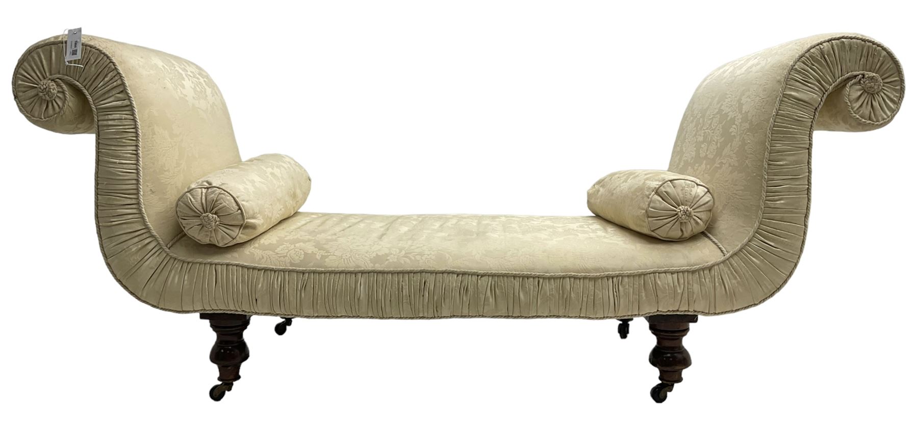 Victorian mahogany framed window seat day bed, the scrolled arms and seat upholstered in ivory foliate patterned damask fabric with matching ropetwist piping, raised on turned supports with castors