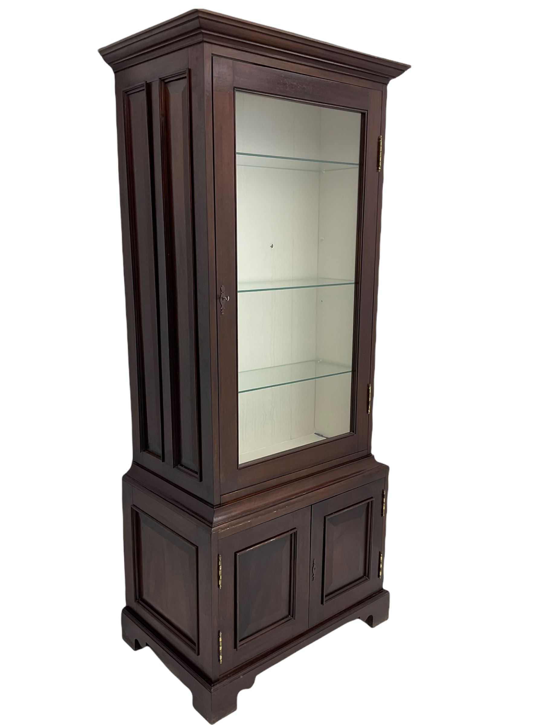 Mahogany display cabinet with hidden compartment, projecting cornice over single glazed door enclosing glass shelves, double panelled cupboard below, the interior with button releasing sliding back compartment, on bracket feet