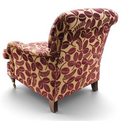 Traditional Howard shape armchair, rolled back and arms over deep seat, raised on turned supports with brass cups and castors, upholstered in plum foliate patterned fabric with loose seat cushion
