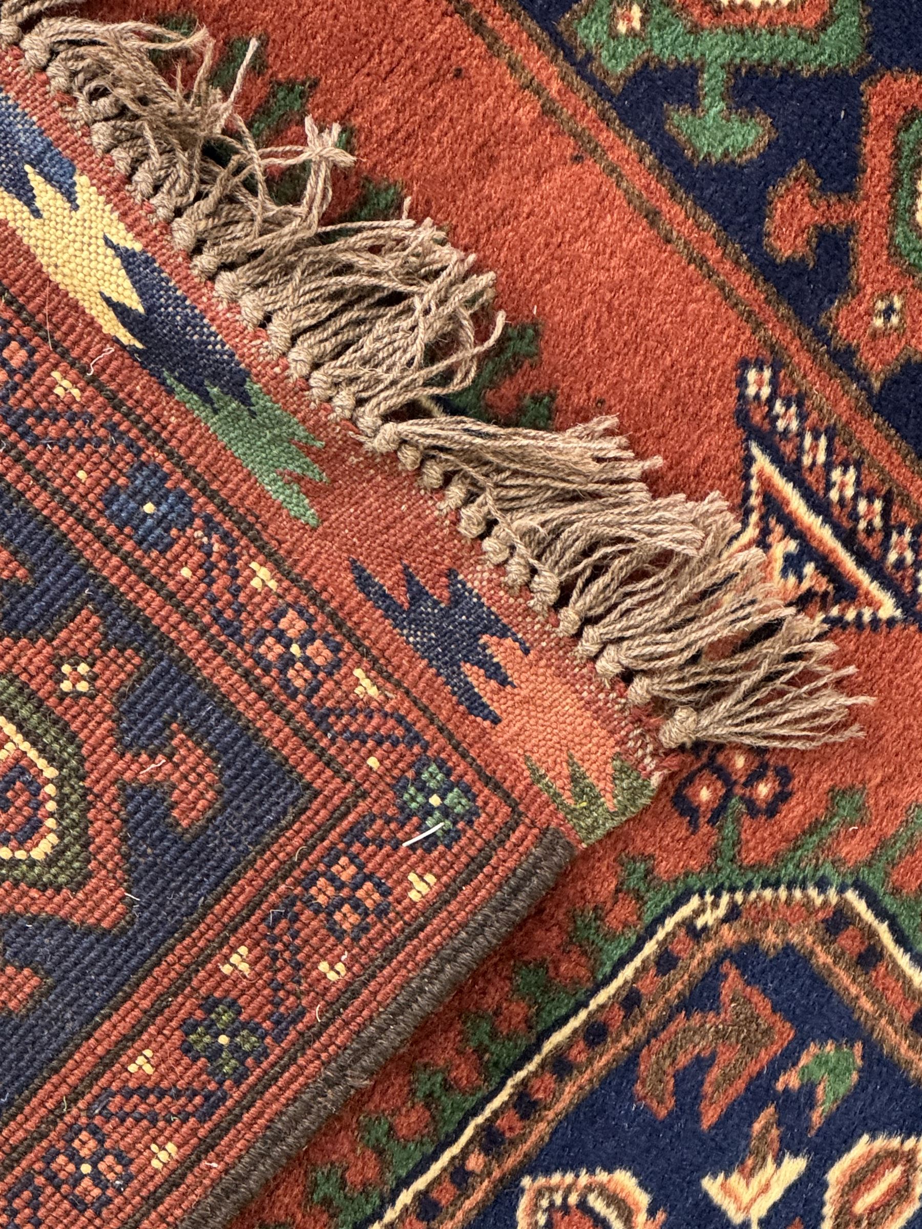 Late 20th century Afghan style ground runner, woven with a repeating panel design along a terracotta field and indigo grounds, framed by multiple narrow borders, and finished with fringed ends