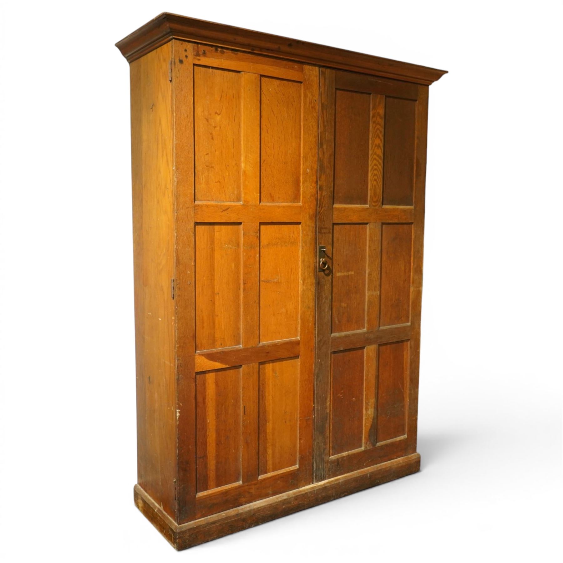 Early 20th century Arts and Crafts oak housekeeper’s cupboard, moulded cornice above pair of panelled doors enclosing a shelved interior, on plinth base