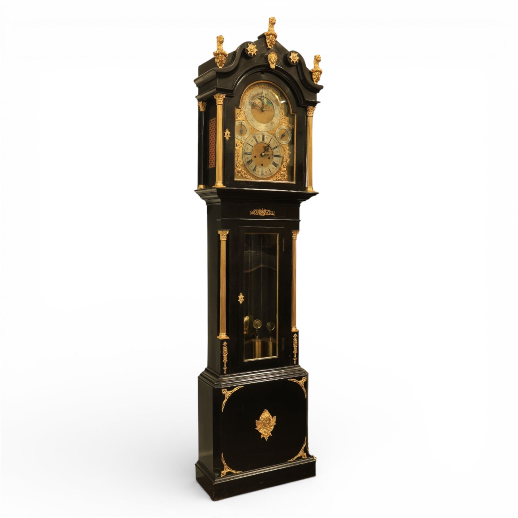 Late nineteenth century ebonised and gilt-bronze mounted musical longcase clock of impressive architectural form, the case of ebonised finish with applied gilt bronze neoclassical inspired masks and mounts, hood of arched form with glazed door, flanked by free fluted columns with gilt bronze Corinthian capitals surmounted by stylized Lion finials, frieze and arch enriched with applied foliate mounts, trunk with a rectangular glazed door bordered by mouldings and flanked by engaged columns with gilt bronze mounts above a shaped projecting base panel with applied central female mask and corner foliate ornamentation, arched brass dial, with a silvered chapter ring and applied cast gilt bronze spandrels and arch decoration, incorporating subsidiary selection dials for chime/silent and tune regulation, offering Cambridge chimes on eight bells and an additional chime sequence on ten bells, brass arch is further embellished with a moon phase aperture with lunar calendar scale, Zodiac symbols, month and date indication on a silvered dial, substantial eight-day, three-train movement with pinned cylinder musical train and a graduated nest of eleven bells with eleven hammers, quarter chiming with separate hour/half-hour strike and chime repetition, movement is regulated by an anchor escapement, with brass disc pendulum, three brass weights, two winding keys and case door key